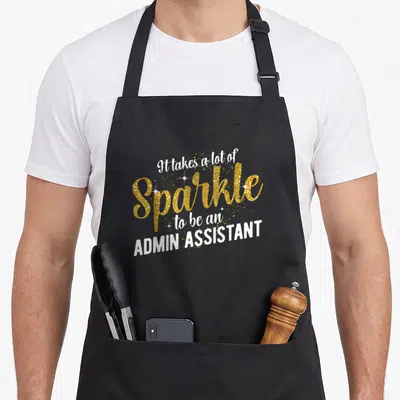 Admin administrative apron - Gold glitter text reading It takes a lot of Sparkle to be an Admin Assistant with white — shown on a black cotton canvas apron against a white background