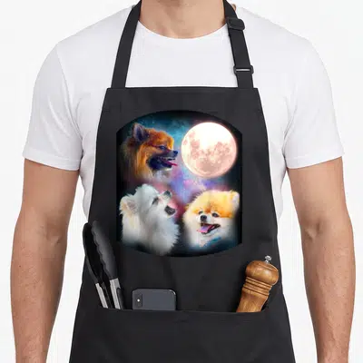 Pomeranian dog apron - Three Pomeranians and full moon against orange white blue purple nebula — shown on a black cotton canvas apron against a white background
