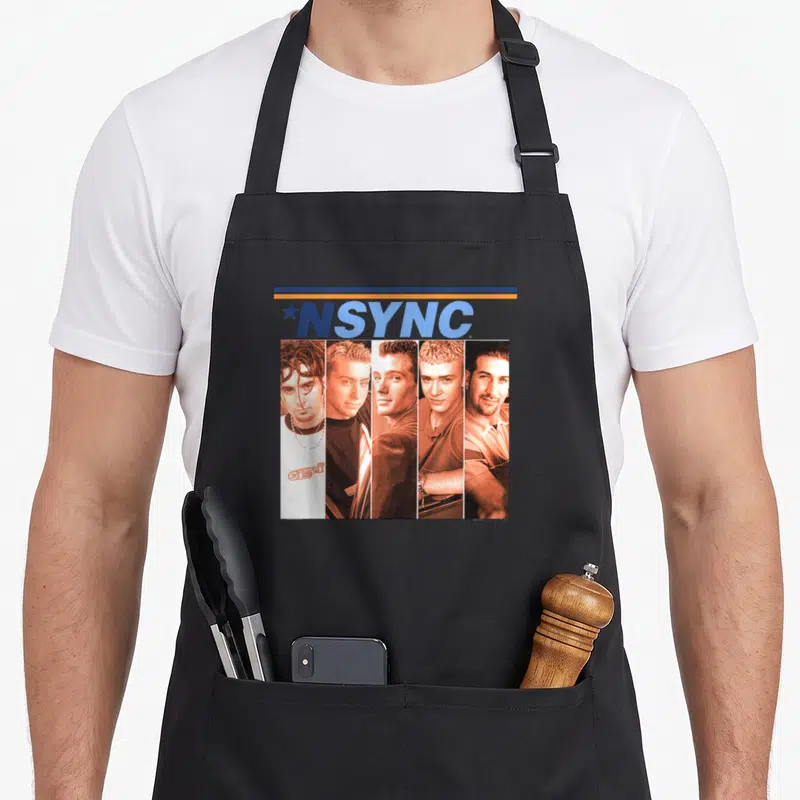 Nsync fandom apron - Five vertical photo strips of men under blue and orange bar with *NSYNC text — shown on a black cotton canvas apron against a white background