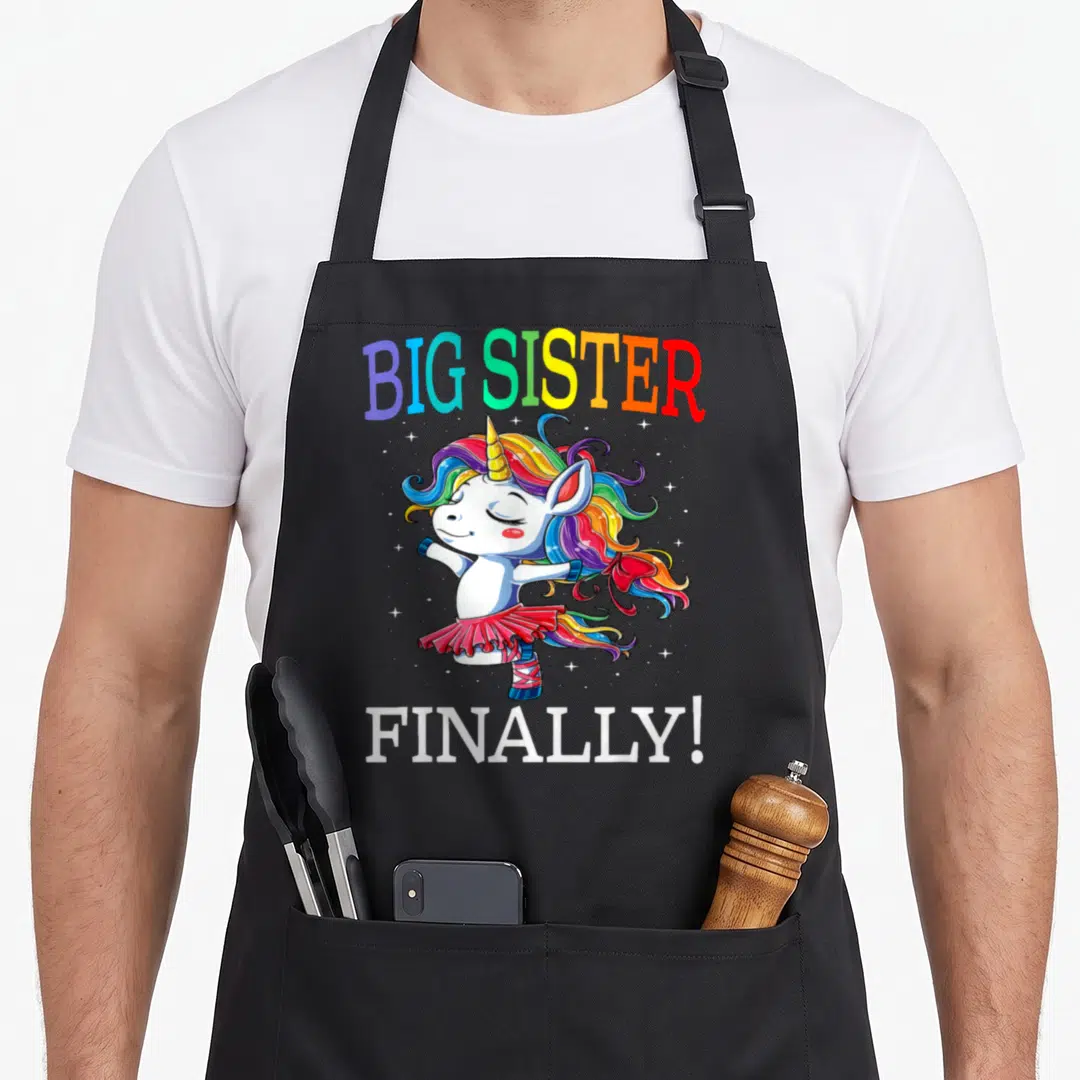 Finally unicorn apron - Rainbow Big Sister Finally text above a white ballerina unicorn with colorful mane and stars — shown on a black cotton canvas apron against a white background