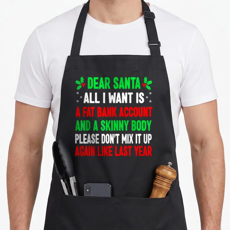 Christmas dear santa apron - Stacked text in green white and red requesting a fat bank account and skinny body flanked — shown on a black cotton canvas apron against a white background