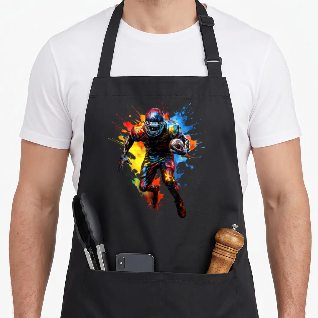 Football paint apron - Watercolor football player running with ball amidst blue red yellow and black splashes — shown on a black cotton canvas apron against a white background