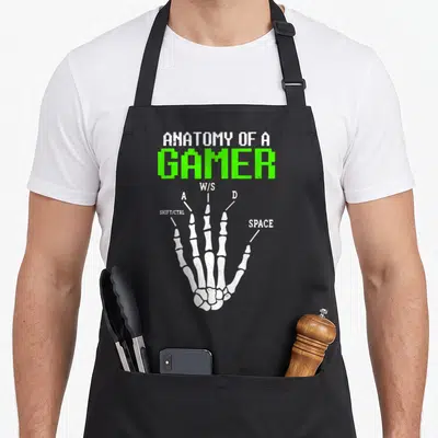 Anatomy gamer skeleton apron - White skeletal hand diagram labeled with W A S D and space bar keys in distressed green — shown on a black cotton canvas apron against a white background