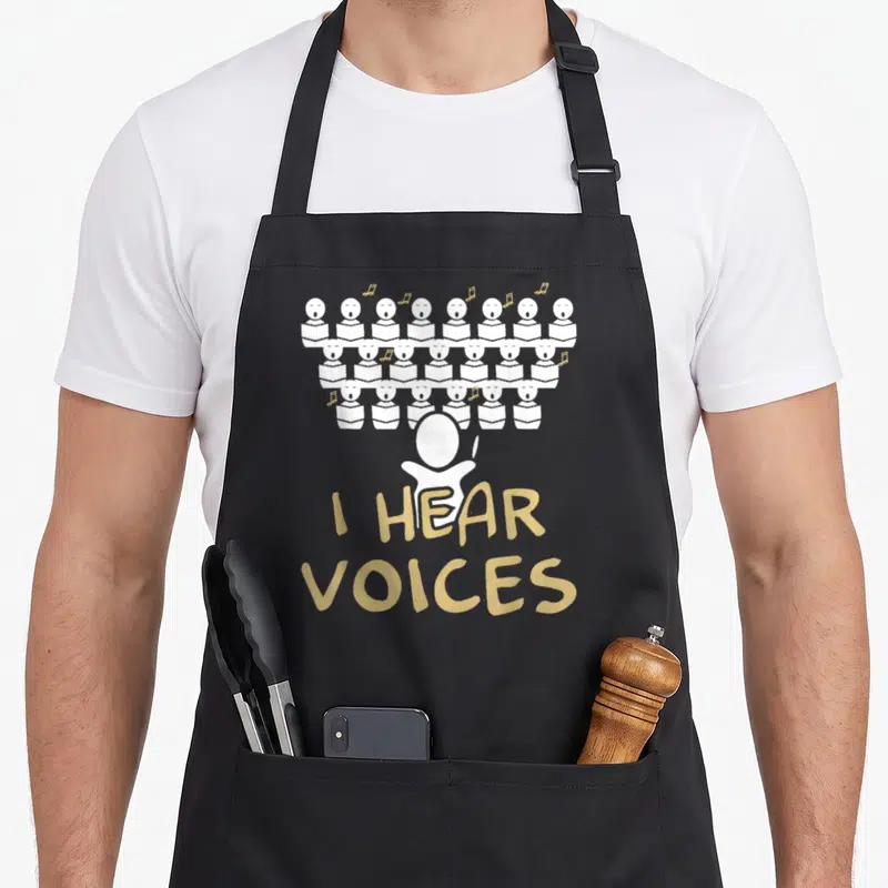 Choir teacher apron - Cartoon choir in three rows above conductor with I HEAR VOICES text — shown on a black cotton canvas apron against a white background