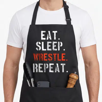 Cool wrestler wrestling apron - Stacked EAT. SLEEP. WRESTLE. REPEAT. text in white and red distressed typography — shown on a black cotton canvas apron against a white background
