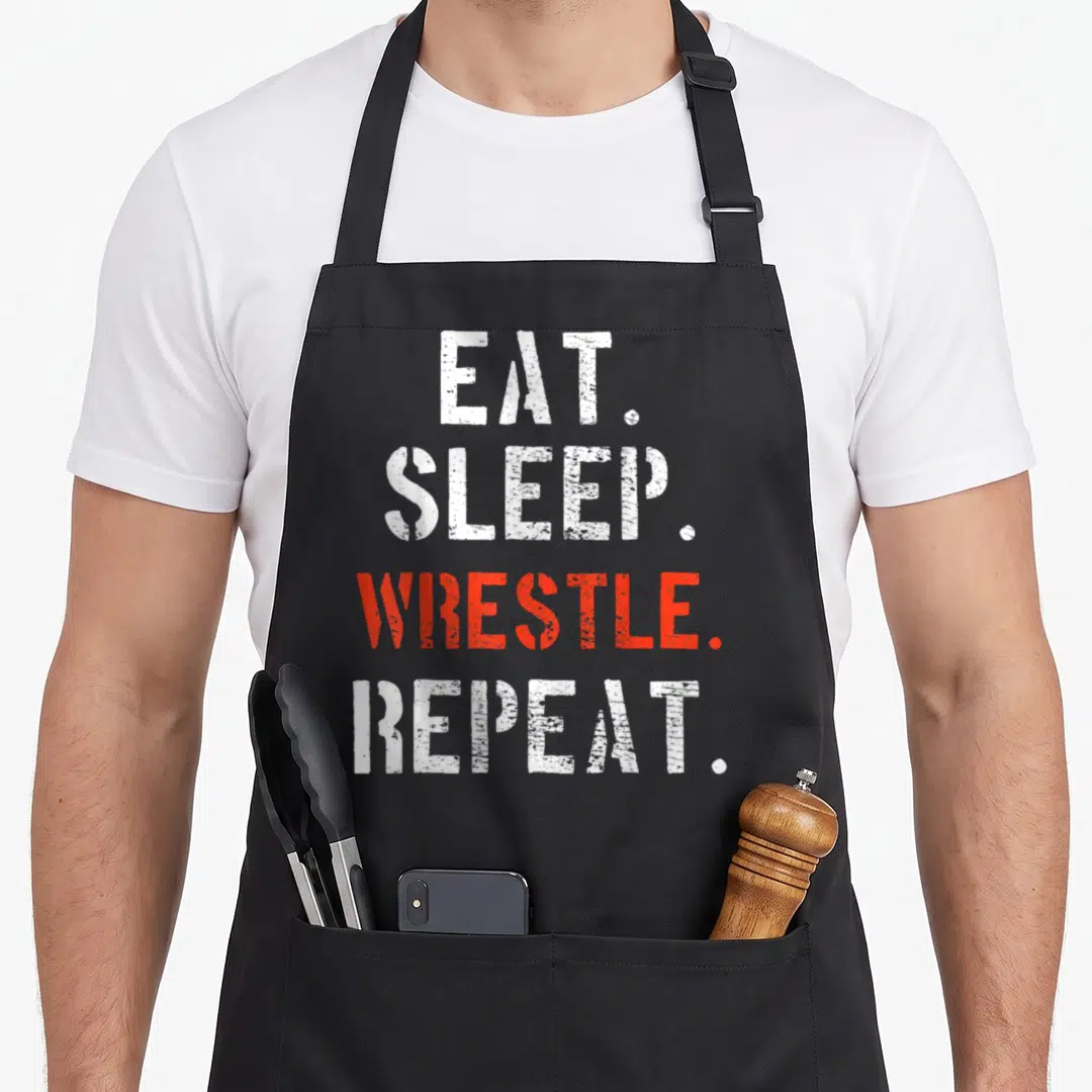 Cool wrestler wrestling apron - Stacked EAT. SLEEP. WRESTLE. REPEAT. text in white and red distressed typography — shown on a black cotton canvas apron against a white background