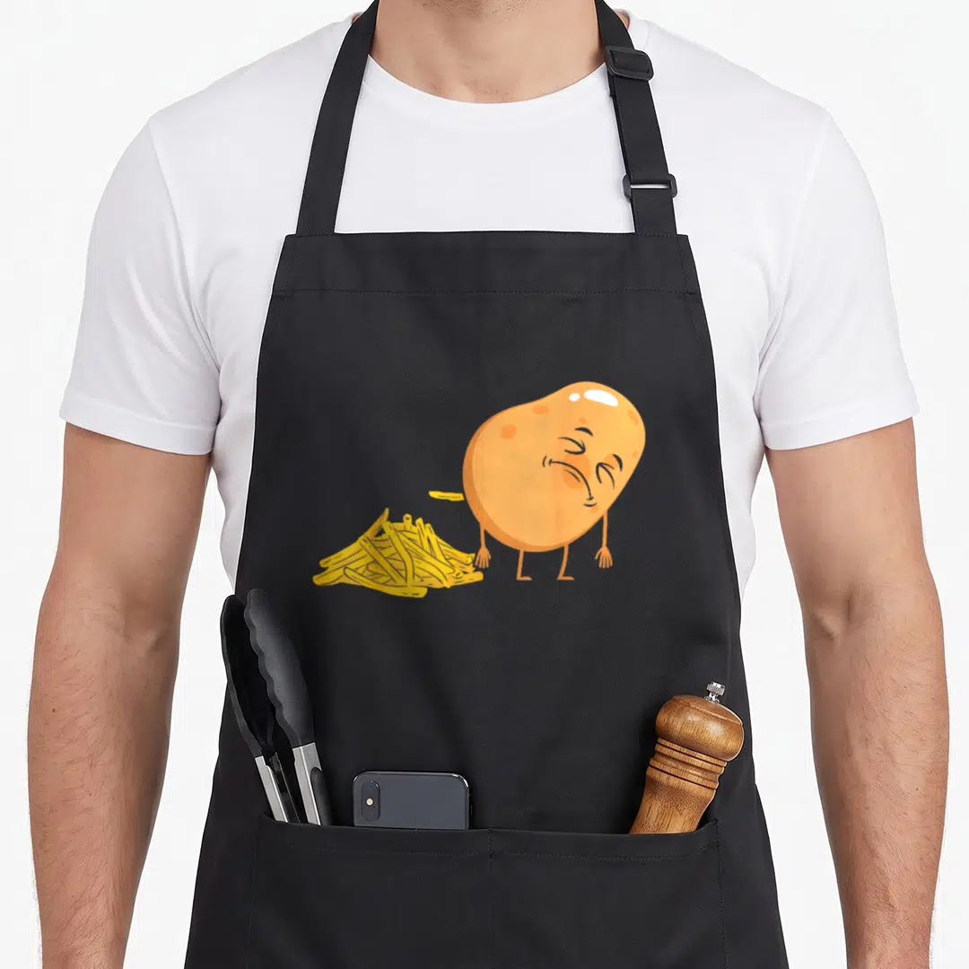 Pooping french apron - Cartoon orange potato standing beside a pile of yellow french fries in a simple art style — shown on a black cotton canvas apron against a white background