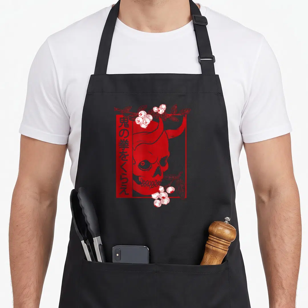 Japanese skull apron - Red oni skull in rectangular frame with vertical kanji and berry branches — shown on a black cotton canvas apron against a white background