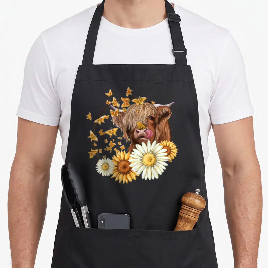 Sunflower highland cow apron - Realistic brown highland cow head in a circle surrounded by orange butterflies and white — shown on a black cotton canvas apron against a white background