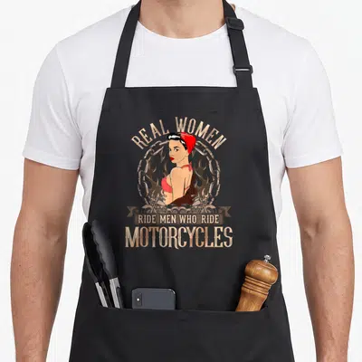 Ride pin up apron - Retro pin-up woman with Real Women Ride Men Who Ride Motorcycles text, chains and flames — shown on a black cotton canvas apron against a white background