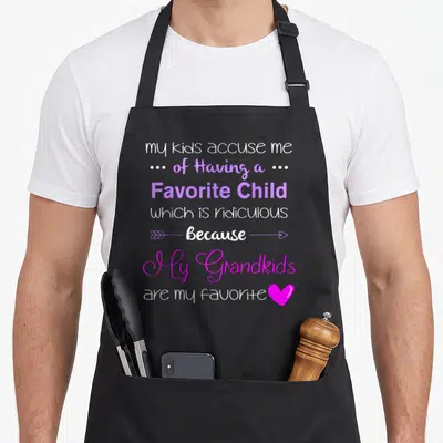 Grandkid grandma apron - Stacked white and purple text reading my grandkids are my favorite with arrows and a pink heart — shown on a black cotton canvas apron against a white background