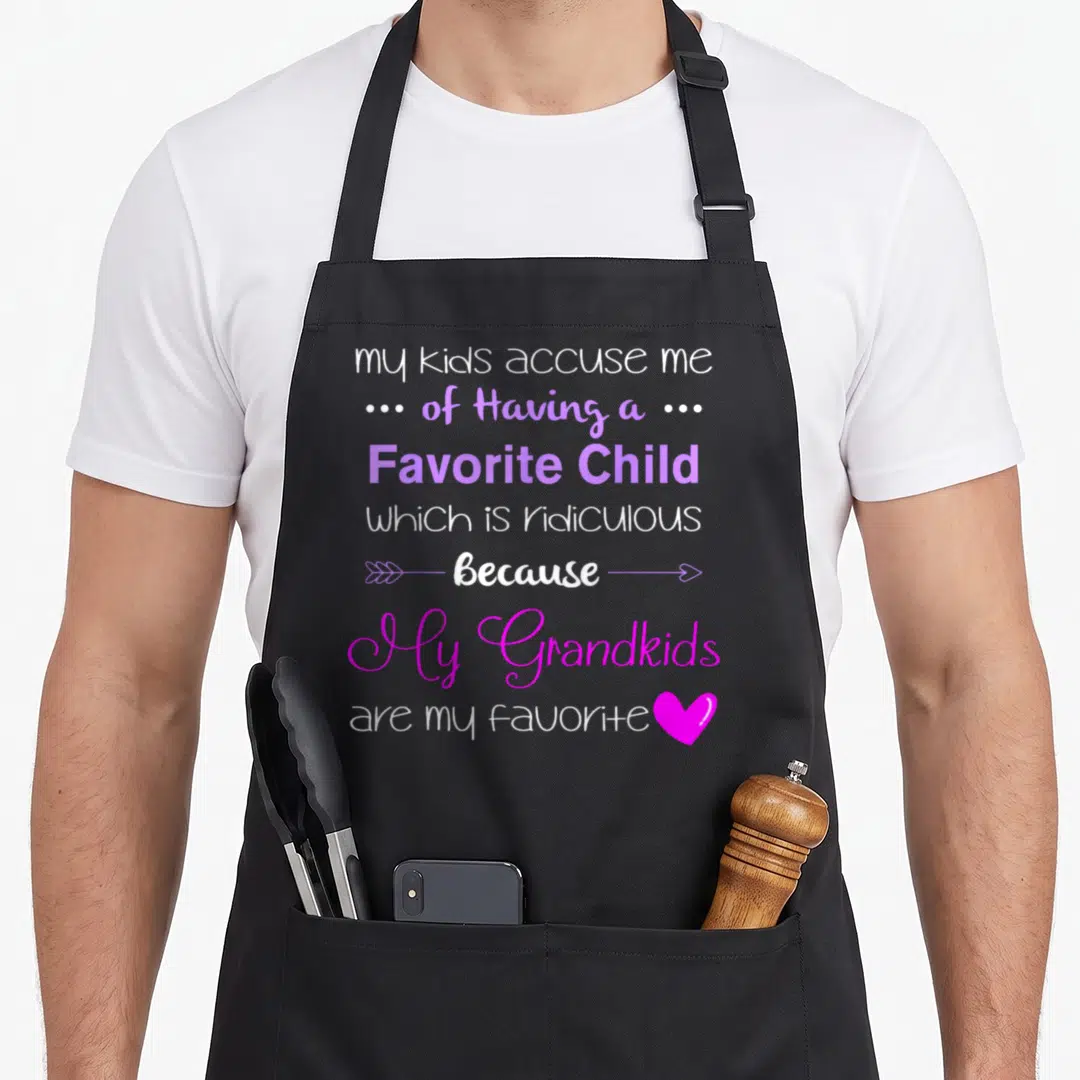 Grandkid grandma apron - Stacked white and purple text reading my grandkids are my favorite with arrows and a pink heart — shown on a black cotton canvas apron against a white background