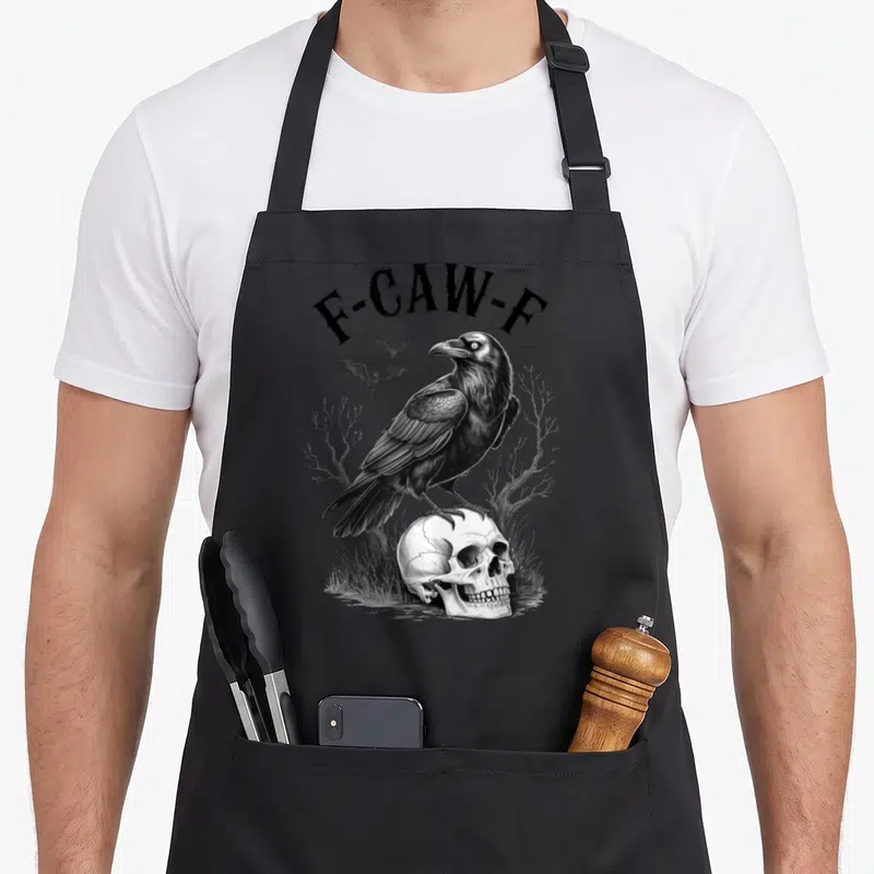 Crow bird aprons - F-CAW-F text over crow on skull with bats and dead trees in grayscale — shown on a black cotton canvas apron against a white background