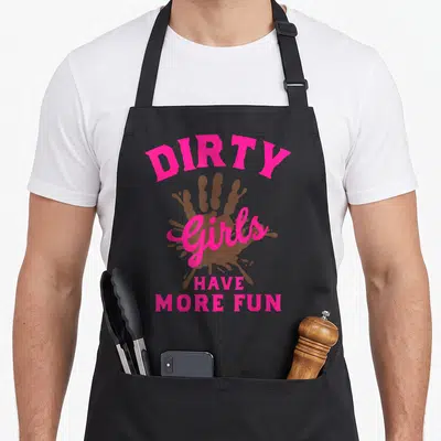 Muddy the dirty apron - Pink text reading Girls Have More Fun above and below a brown handprint graphic — shown on a black cotton canvas apron against a white background