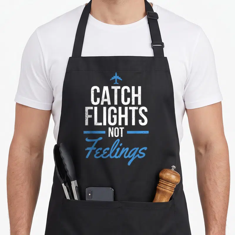 Catch flight crew apron - Blue airplane icon above white and blue text reading CATCH FLIGHTS NOT Feelings — shown on a black cotton canvas apron against a white background