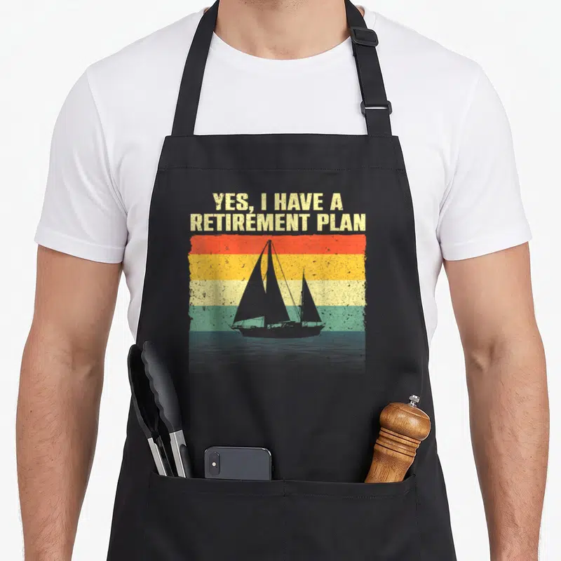Sailing retirement apron - Retro sailboat silhouette over red orange yellow and green stripes with stacked beige text — shown on a black cotton canvas apron against a white background