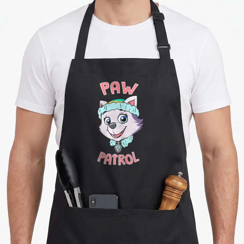 Everest face apron - Cartoon dog head between PAW and PATROL text in pink and blue — shown on a black cotton canvas apron against a white background