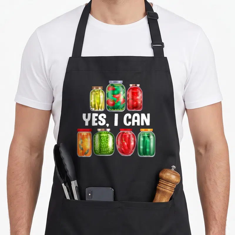 Preserving canning apron - Seven jars of pickled vegetables surrounding white YES, I CAN text — shown on a black cotton canvas apron against a white background