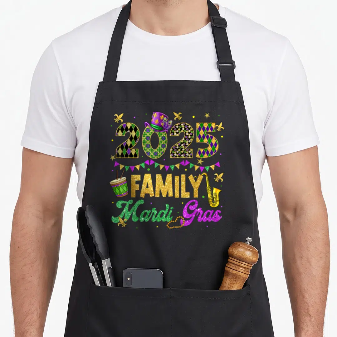 Family fat chef apron - 2025 FAMILY Mardi Gras design with drum saxophone beads and fleur-de-lis in purple green gold — shown on a black cotton canvas apron against a white background