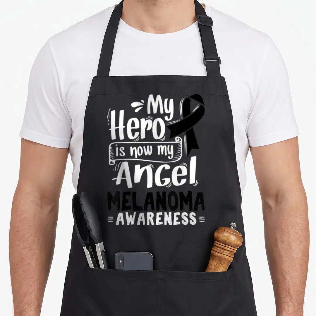 Malignant ribbon apron - White My Hero is now my Angel text with black ribbon and Melanoma Awareness lettering — shown on a black cotton canvas apron against a white background