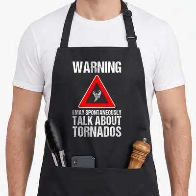 Storm hunter apron - Distressed warning sign with red triangle and text I may spontaneously talk about tornados — shown on a black cotton canvas apron against a white background