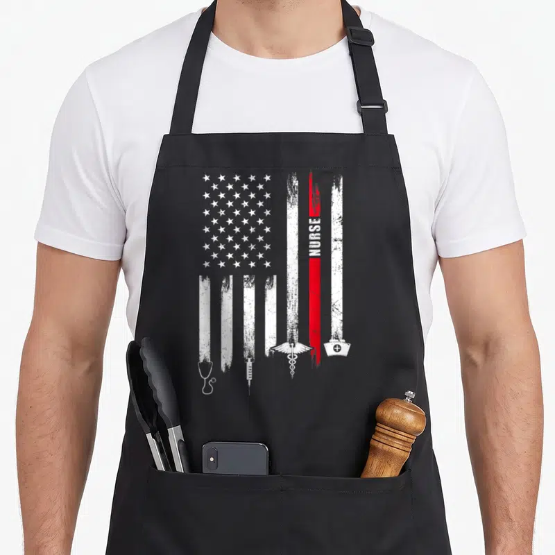 Flag nurse apron - Distressed white and red flag with vertical NURSE text and bottom row of medical icons — shown on a black cotton canvas apron against a white background
