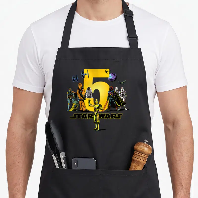 Character fifth birthday apron - Yellow number 5 with Star Wars characters and starships in cartoon art — shown on a black cotton canvas apron against a white background