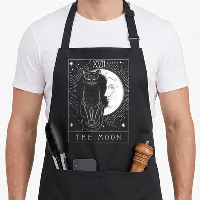 Tarot cat apron - White line art of cat and face moon with XVII and THE MOON text in rectangular border — shown on a black cotton canvas apron against a white background