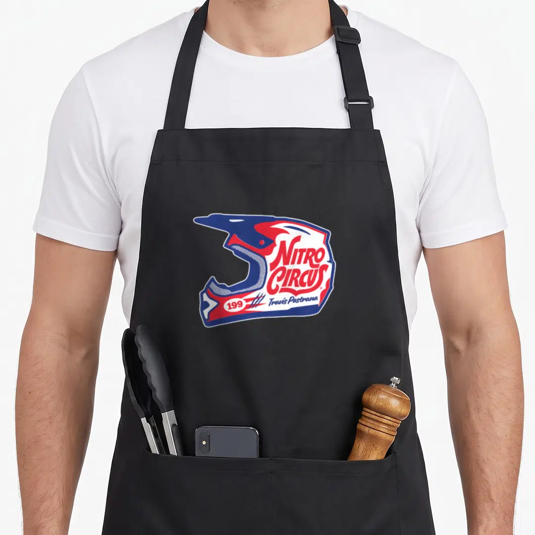 Nitro circus apron - Blue red and white helmet graphic with Nitro Circus text and Travis Pastrana name — shown on a black cotton canvas apron against a white background