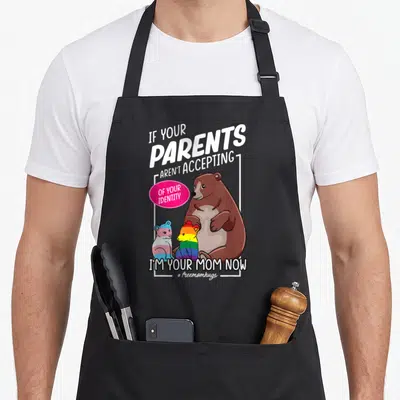 Free mother's apron - Brown bear with rainbow and trans flag colored cubs and identity acceptance text — shown on a black cotton canvas apron against a white background