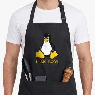 Mascot penguin aprons - Cartoon penguin sitting above yellow I AM ROOT text in black and white — shown on a black cotton canvas apron against a white background