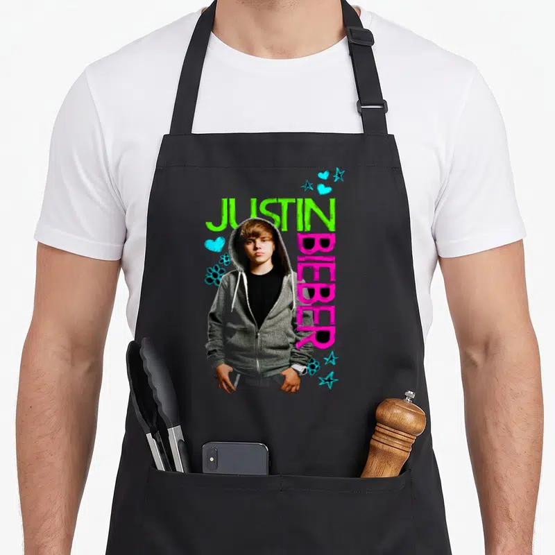 Justin black apron - Photo of Justin Bieber in grey hoodie with green and pink text and blue decorative shapes — shown on a black cotton canvas apron against a white background