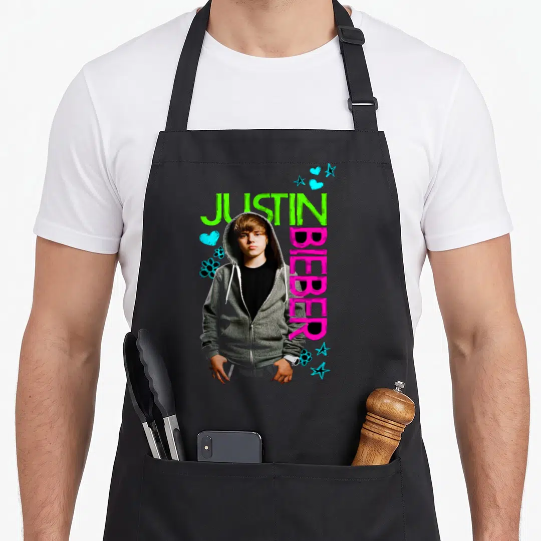Justin black apron - Photo of Justin Bieber in grey hoodie with green and pink text and blue decorative shapes — shown on a black cotton canvas apron against a white background