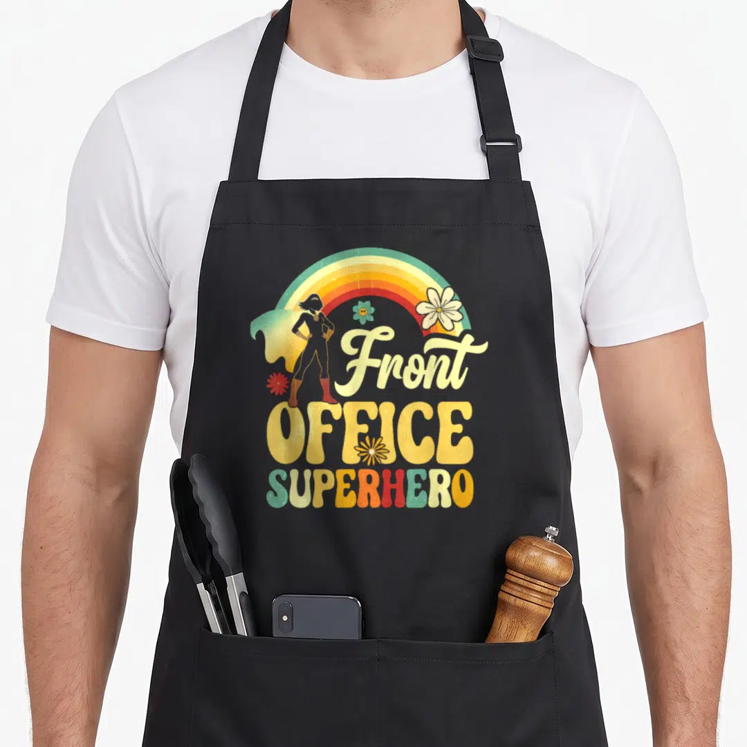 Office superhero apron - Retro superhero silhouette under rainbow arch with Front Office Superhero text and flowers — shown on a black cotton canvas apron against a white background