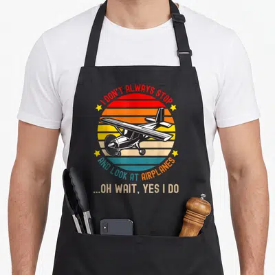 Alway airplane apron - Retro airplane over striped sunburst with text I don't always stop look at airplanes oh wait yes — shown on a black cotton canvas apron against a white background
