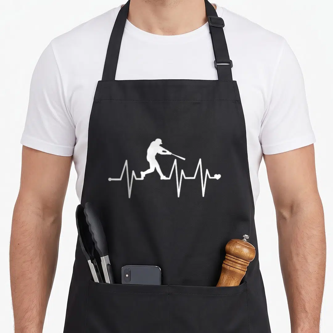 Pulse baseball apron - white batter silhouette inside a heartbeat line ending in a small heart — shown on a black cotton canvas apron against a white background