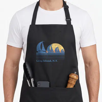 Island 80s apron - Four blue sailboats on yellow sun with Long Island N.Y. text — shown on a black cotton canvas apron against a white background