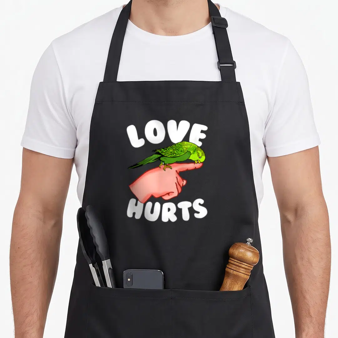 Pet budgie bird apron - Green parrot perched on pink finger with white LOVE HURTS text — shown on a black cotton canvas apron against a white background