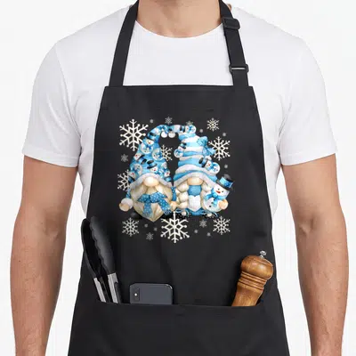 Gnomy snowman apron - Two gnomes with blue striped hats forming a heart surrounded by snowmen and snowflakes — shown on a black cotton canvas apron against a white background