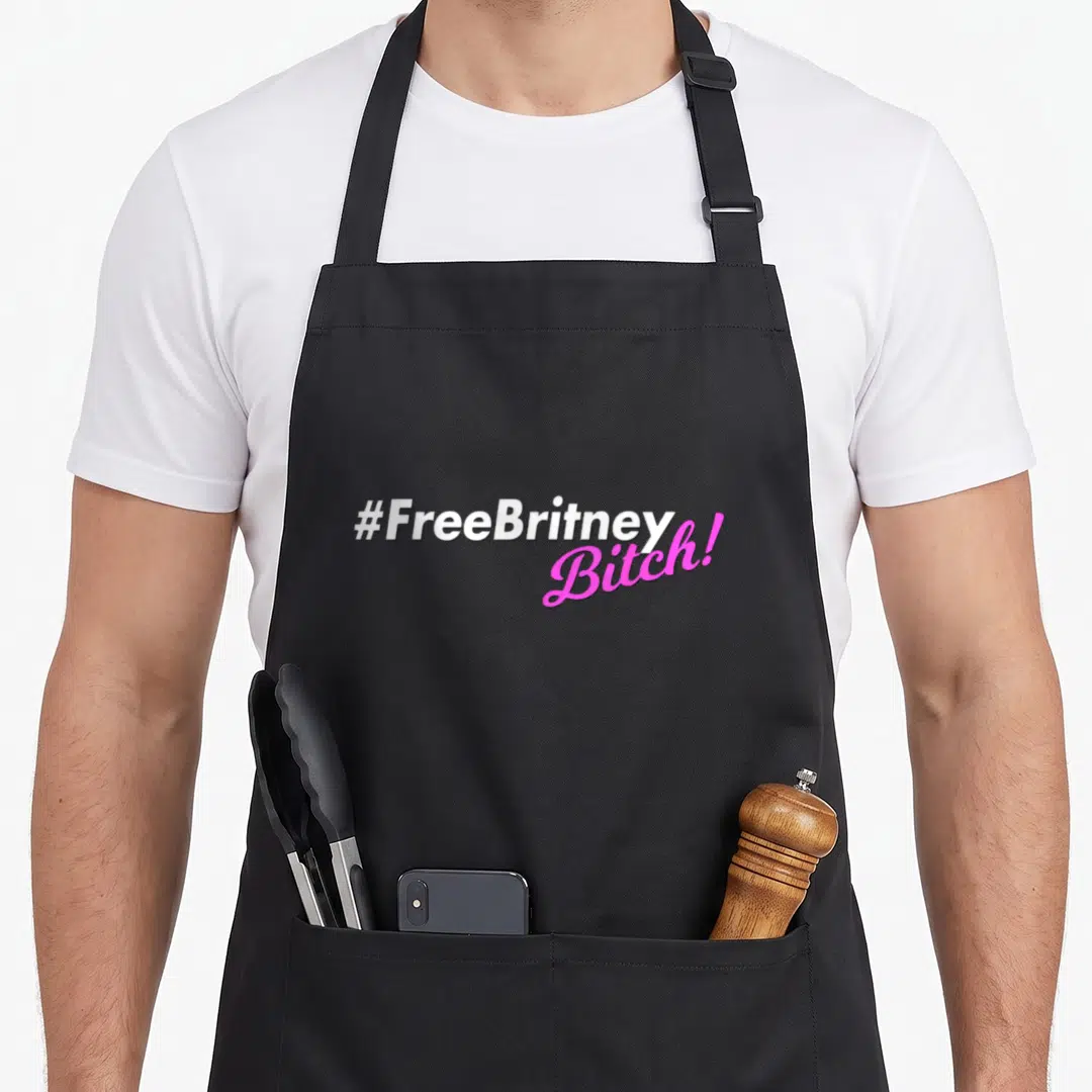 Freebritneybitch brittany apron - Stacked white and pink text reading #FreeBritney Bitch! on black fabric — shown on a black cotton canvas apron against a white background