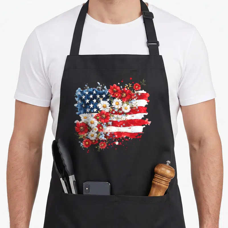 Wildflower 4th of july apron - Watercolor USA flag intertwined with red white flowers and green leaves — shown on a black cotton canvas apron against a white background