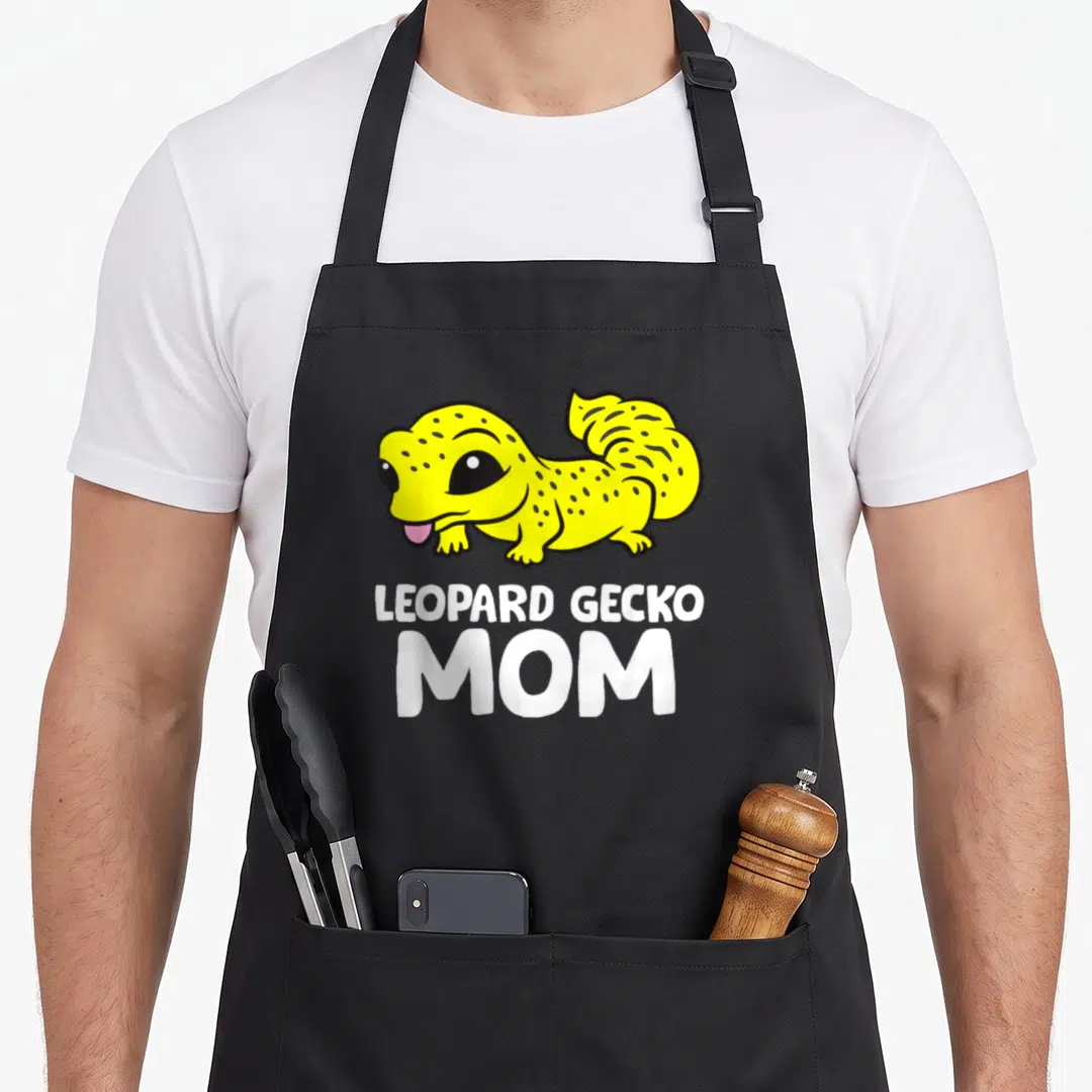 Animal leopard apron - Yellow cartoon gecko with black spots above white LEOPARD GECKO MOM text — shown on a black cotton canvas apron against a white background