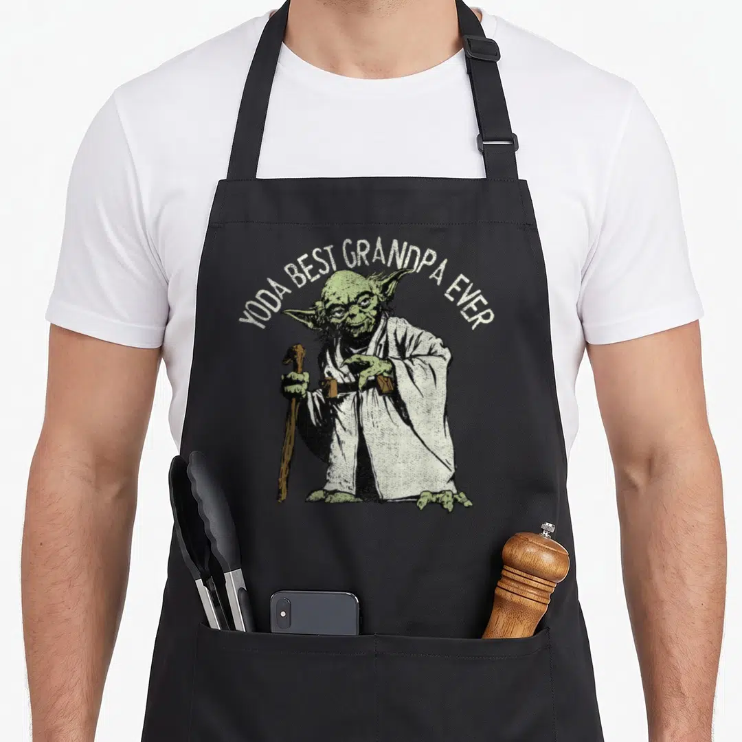 Yoda grandpa apron - Arched YODA BEST GRANDPA EVER text over green character holding brown cane in distressed white — shown on a black cotton canvas apron against a white background