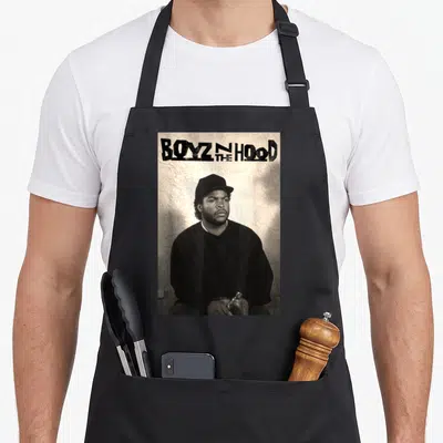 Boyz mean apron - BOYZ N THE HOOD text above seated man in cap holding bottle — shown on a black cotton canvas apron against a white background