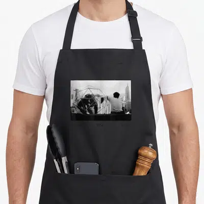 Someone mary apron - Black and white photo of a man near a wireframe structure with three columns of text below — shown on a black cotton canvas apron against a white background