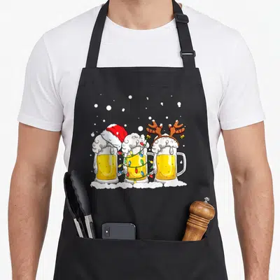 Beer christmas tree apron - Three cartoon beer mugs with Santa hat, reindeer antlers, and Christmas lights on snow — shown on a black cotton canvas apron against a white background