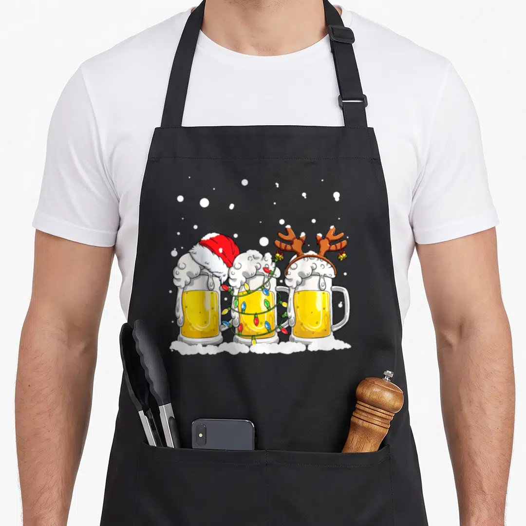 Beer christmas tree apron - Three cartoon beer mugs with Santa hat, reindeer antlers, and Christmas lights on snow — shown on a black cotton canvas apron against a white background