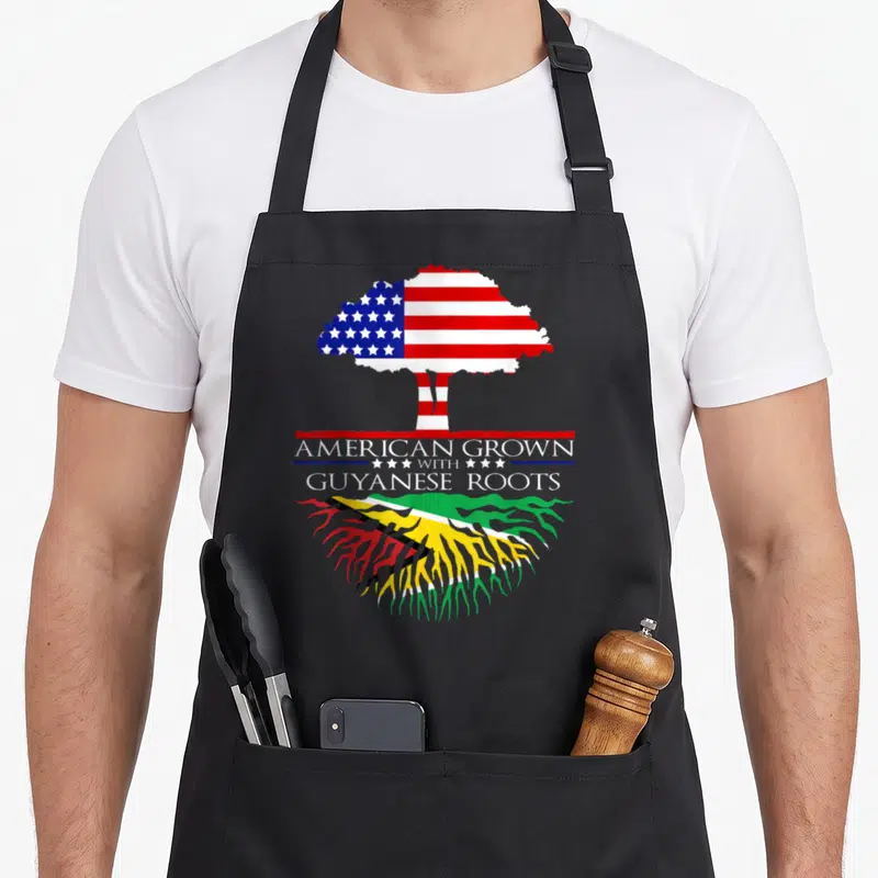 Guyanese african american aprons - Tree with US flag canopy and Guyanese roots flanking stacked text — shown on a black cotton canvas apron against a white background