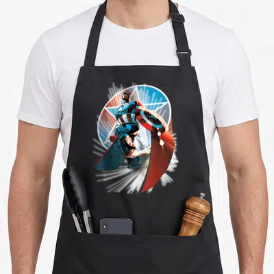 Hand falcon apron - Realistic Captain America in blue and red holding shield over white star graphic — shown on a black cotton canvas apron against a white background