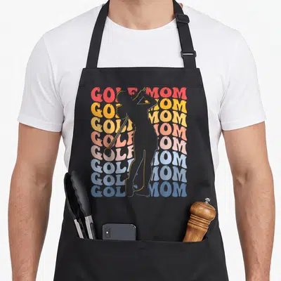 Groovy golf apron - Grey golfer silhouette swinging club over eight rainbow GOLF MOM text lines — shown on a black cotton canvas apron against a white background